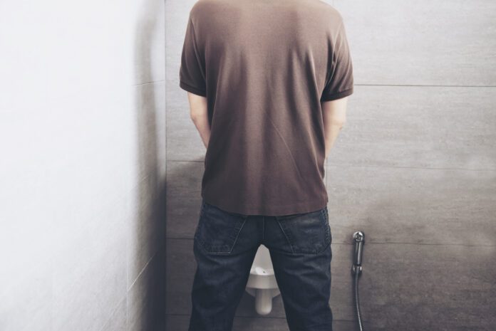 mans-back-as-he-pees-in-public-urinal-against-white-tiles