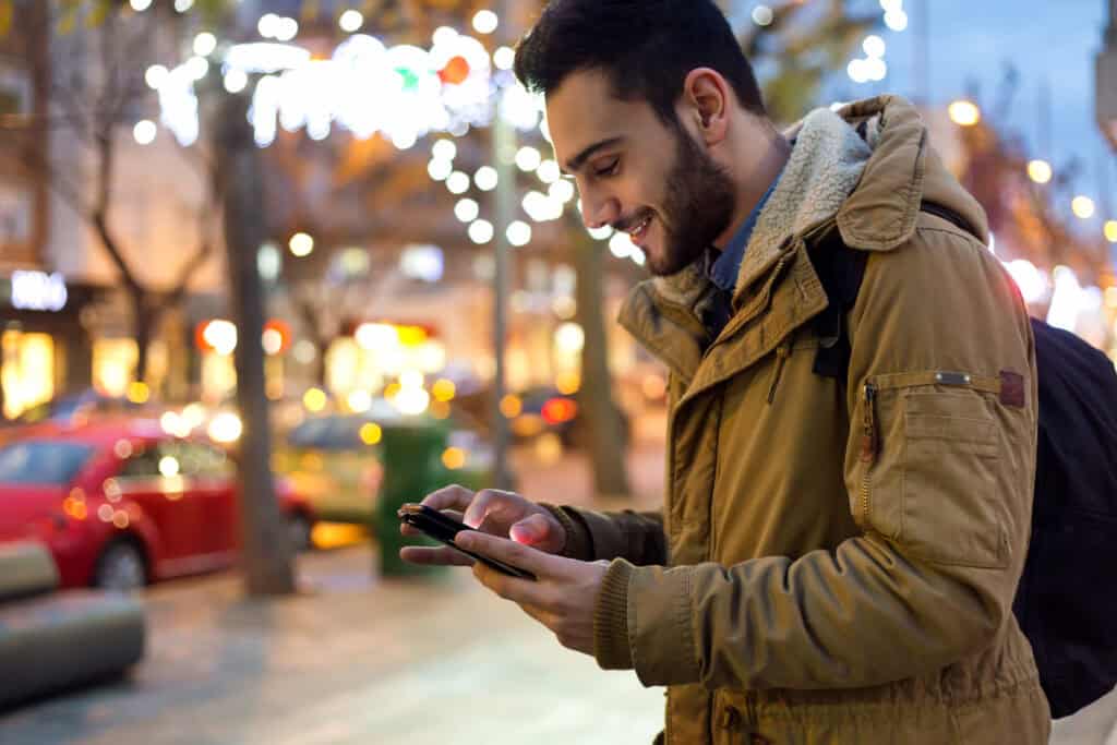photo-of-a-young-man-with-a-beard-using-his-phone-in-the-street-and-smiling-because-he-is-getting-to-use-a-fast-network-with-Lyca-prepaid-SIM