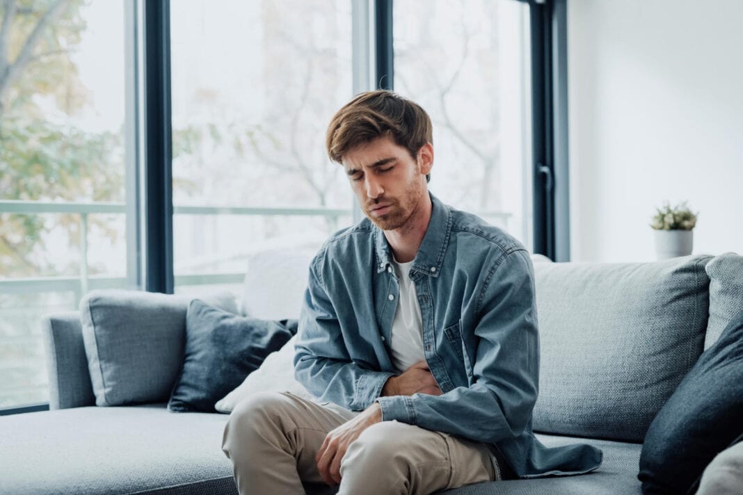 photo-of-man-sitting-on-couch-clutching-stomach-with-stomach-ache
