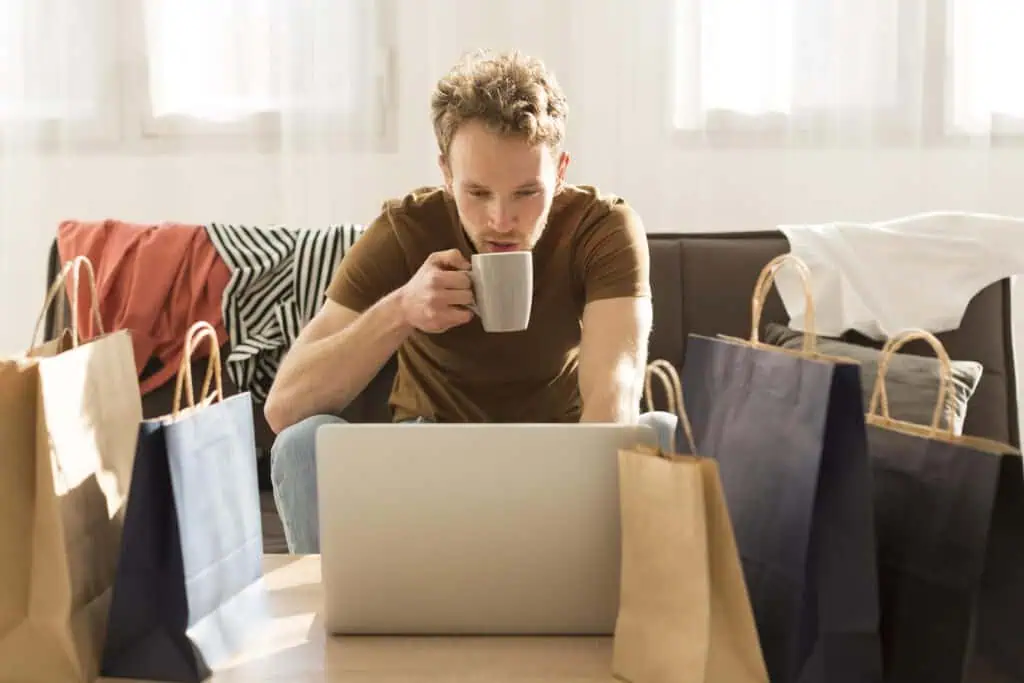 man-surrounded-by-bags-drinking-coffee-shopping-online