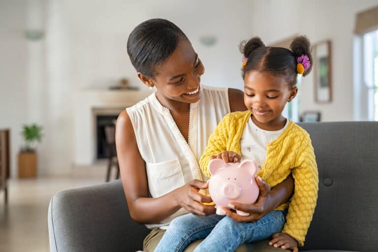 photo-of-mother-and-daughter-sitting-on-couch-putting-a-coin-in-piggy-bank-to-teach-about-money-in-the-netherlands