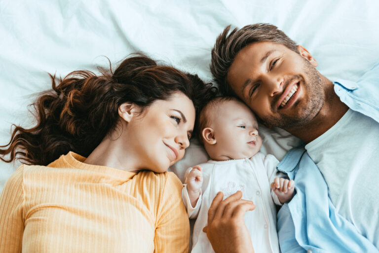 Mother-and-father-on-bed-in-the-Netherlands-with-their-baby-looking-happy