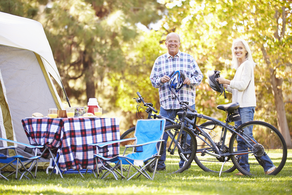 older-couple-taking-a-break-on-their-cycling-vacation-perparing-food-and-camping