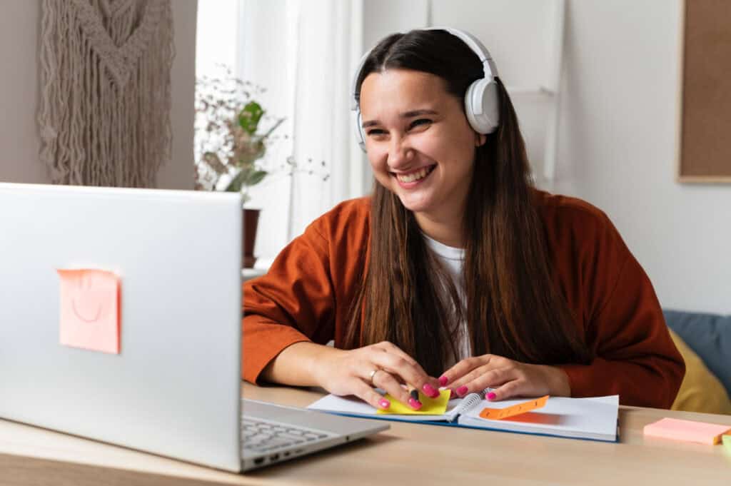 foto-de-mulher-alegre-fazendo-uma-aula-online-no-laptop-com-notas-adesivas-perto