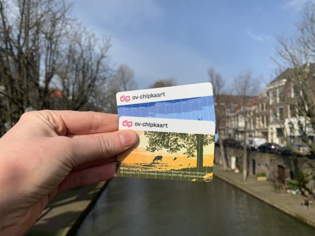 photo-of-personal-and-anonymous-ov-chip-cards-held-up-background-utrecht-canal-houses-water