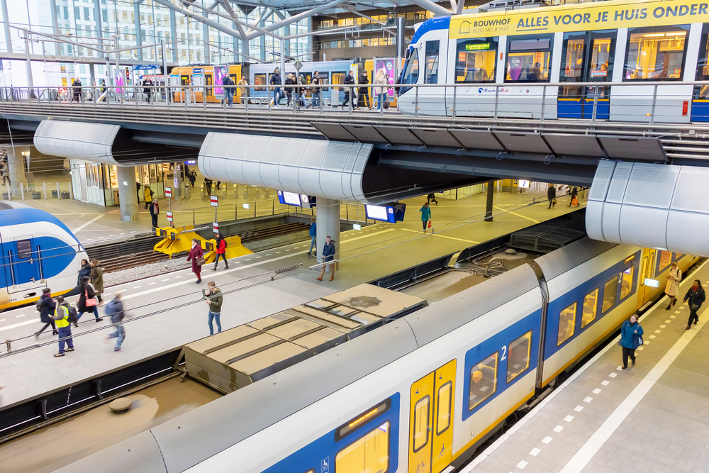 overhead-tram-passing-ns-train-and-commuters-in-busy-den-haag-the-hague-station-netherlands