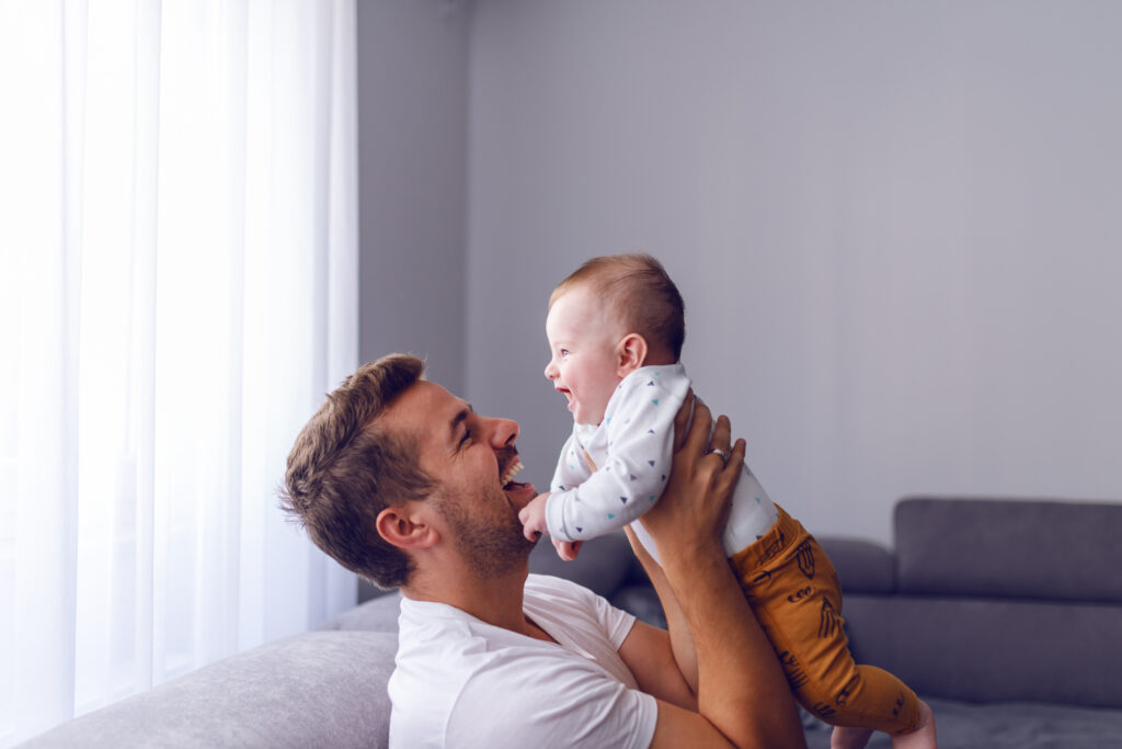 photo-of-a-young-dad-sitting-on-a-couch-and-cuddling-his-baby