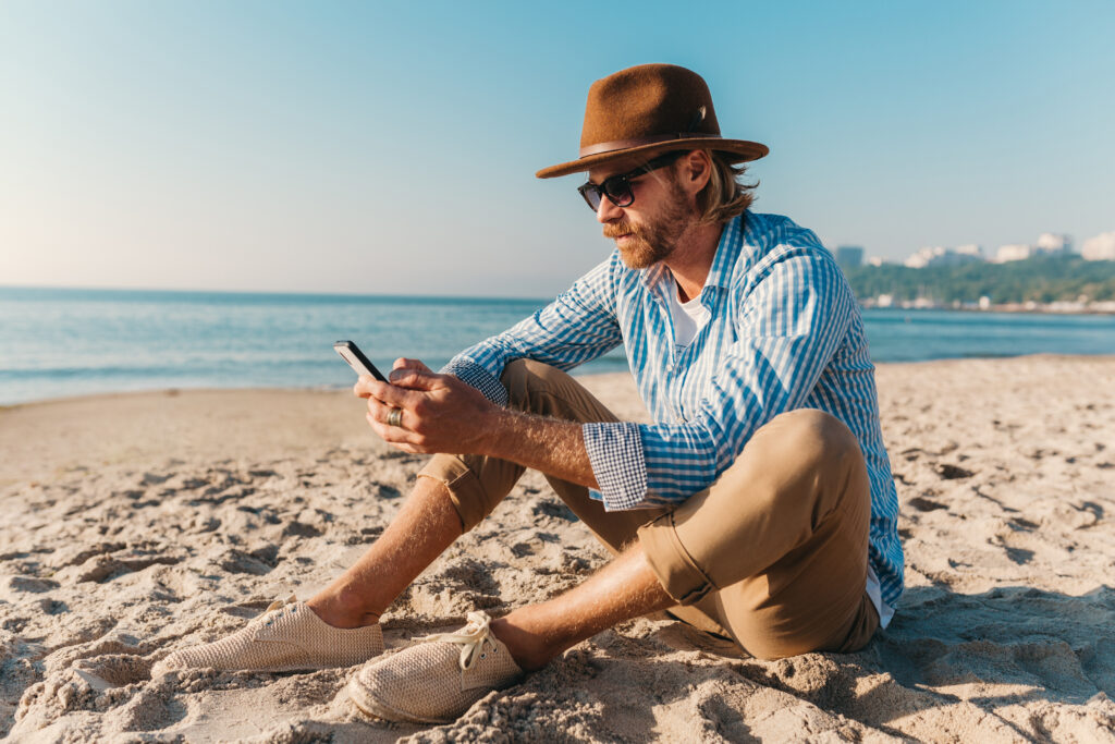 photograph-of-a-man-scrolling-on-his-mobile-phone-whilst-at-the-beach