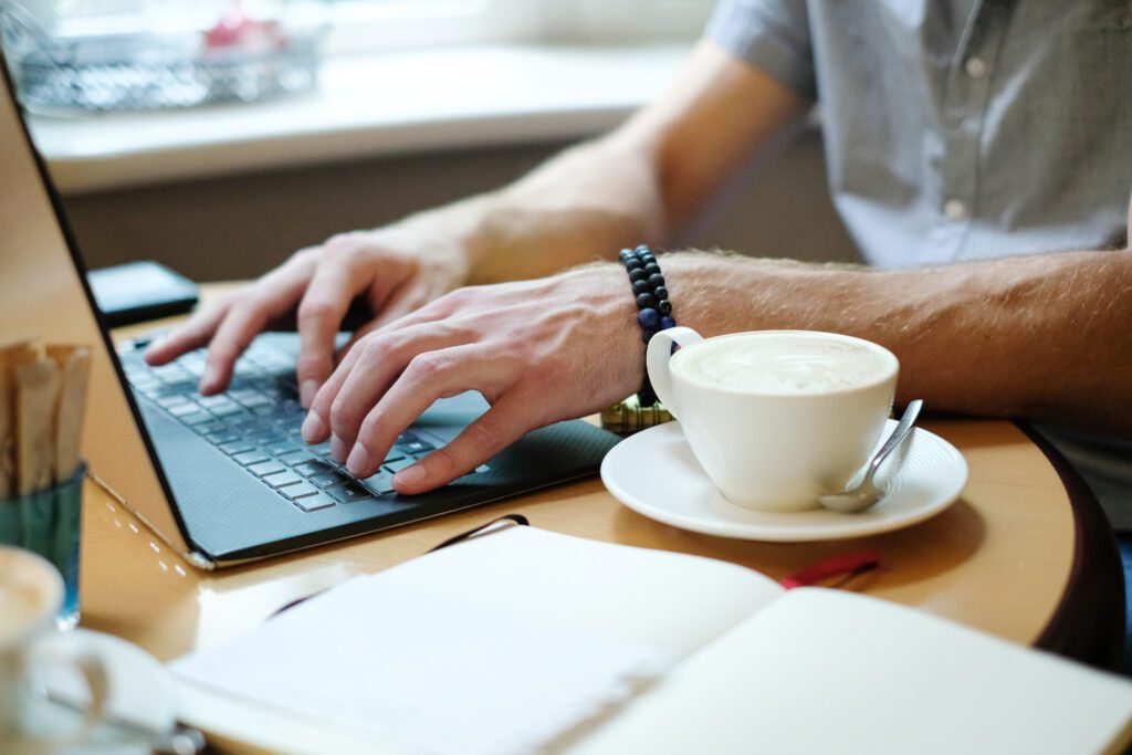photograph-of-a-freelancer-typing-on-his-laptop-with-cup-of-coffee-and-open-notebook-by-his-side