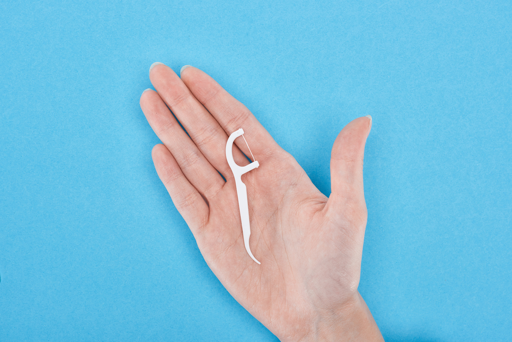 photo-of-hand-against-blue-background-holding-plastic-dental-floss