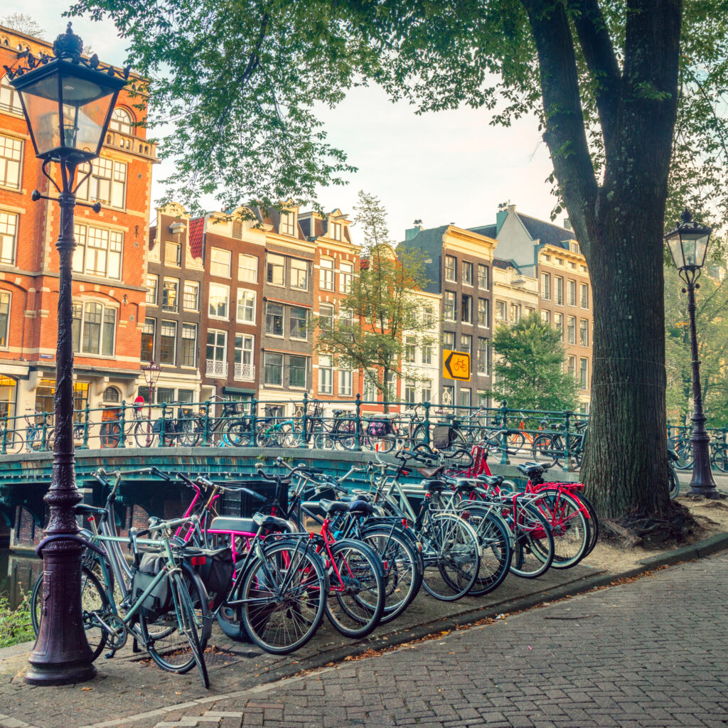 Bikes-lining-an-Amsterdam-canal-with-houses-and-bridge-in-the-background