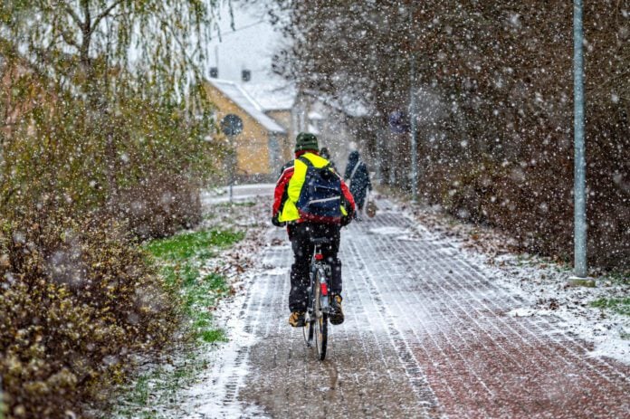 photo-of-cyclist-cycling-down-paved-road-in-high-vis-vest-with-snow