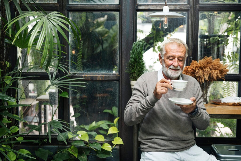 photo-of-retired-dutch-man-drinking-tea-with-AOW-funds-green-background-happy-face-gray-sweater