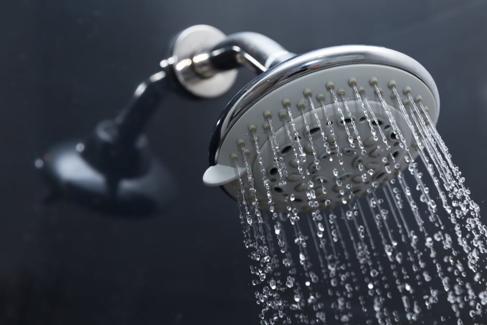 shower-head-in-bath-against-grey-bathroom-tiles-with-water-droplets-coming-out-of-it