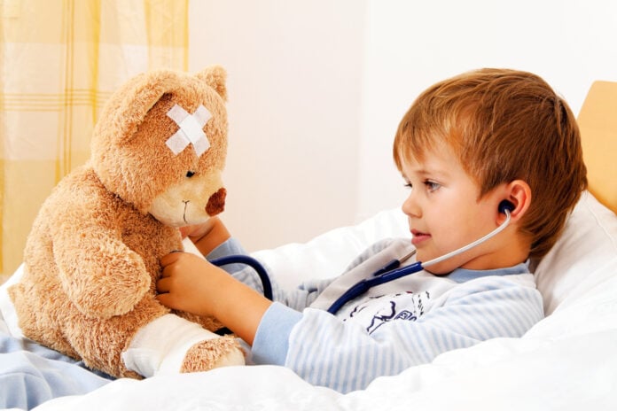 young-boy-laying-sick-in-bed-examining-a-teddy-bear-with-a-stetoscope