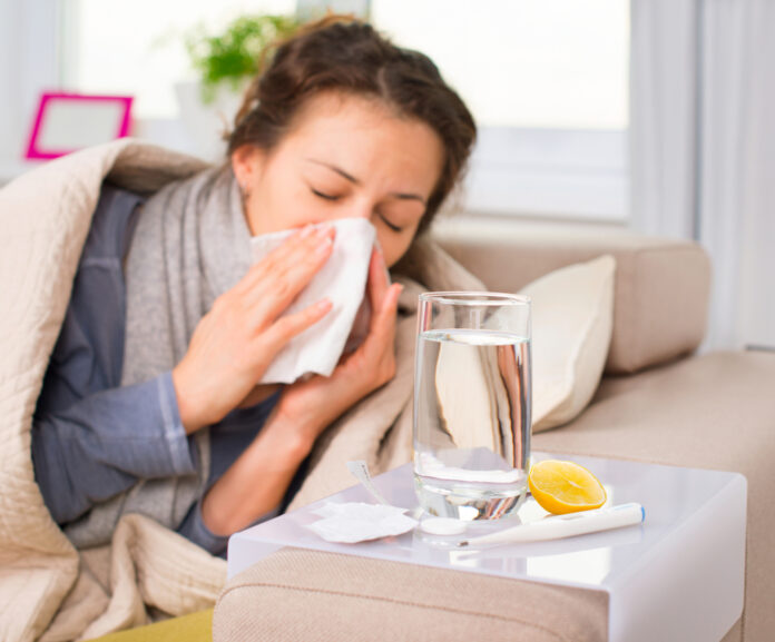 sick-woman-sneezing-in-bed-next-to-glass-of-water-and-lemon