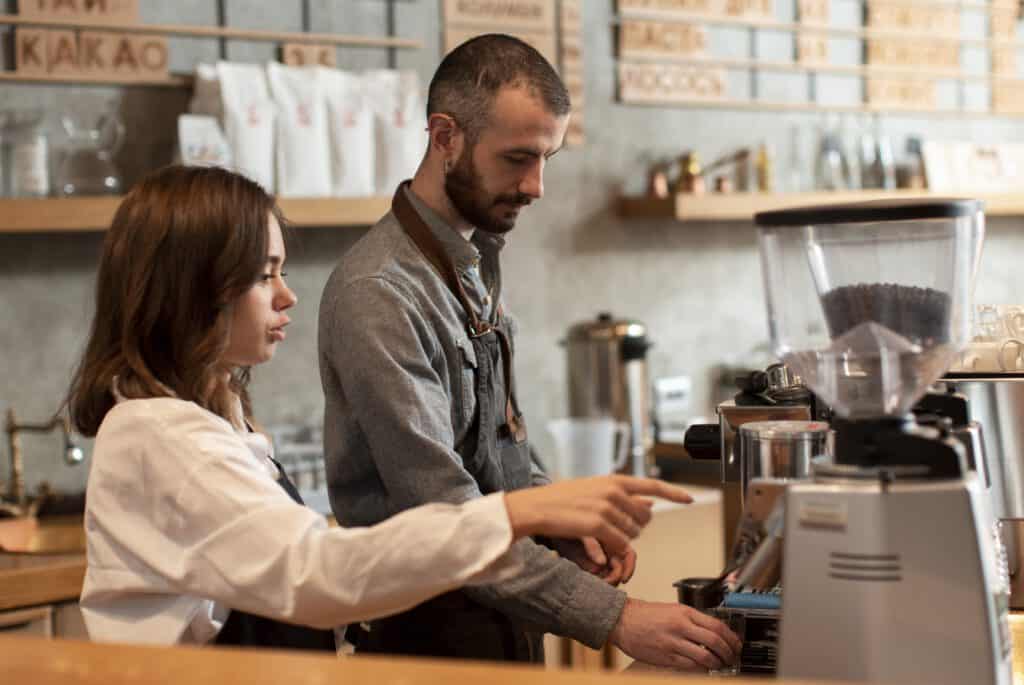 side-view-teenage-girl-working-first-job-at-coffee-shop-being-taught-by-colleague