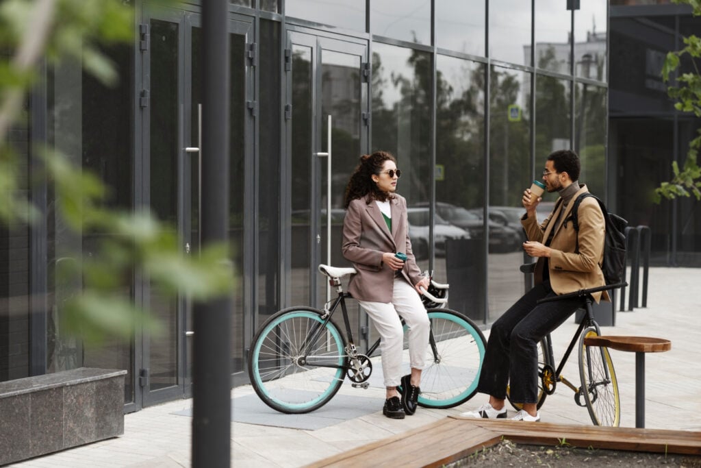 photo-of-two-business-workers-in-the-netherlands-on-sponsored-visa-sitting-on-bikes-outside-office-building-drinking-coffee