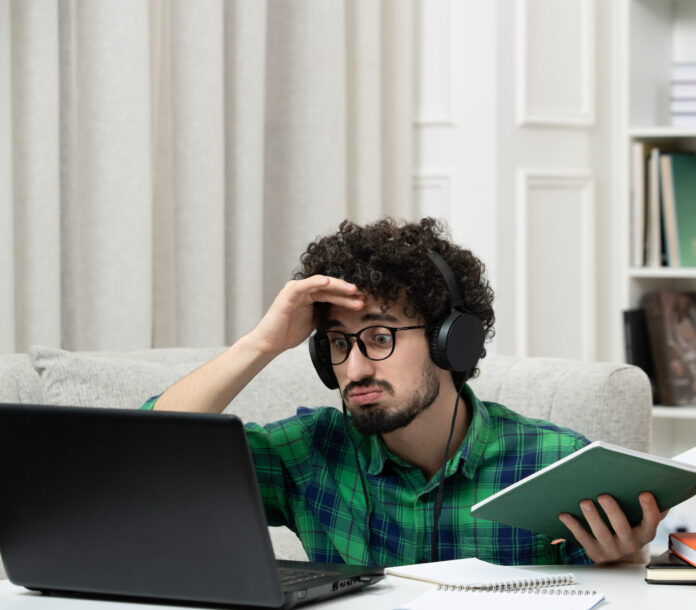 photo-of-student-in-distress-looking-at-laptop-holding-head-in-hands-surrounded-by-books