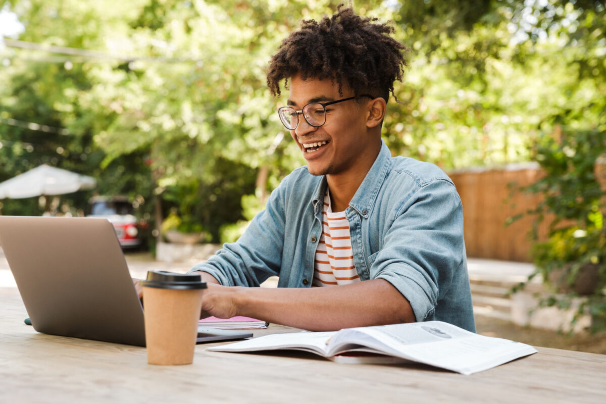 photo-of-black-man-studying-for-knm-exam-at-laptop-smiling-with-trees-in-background