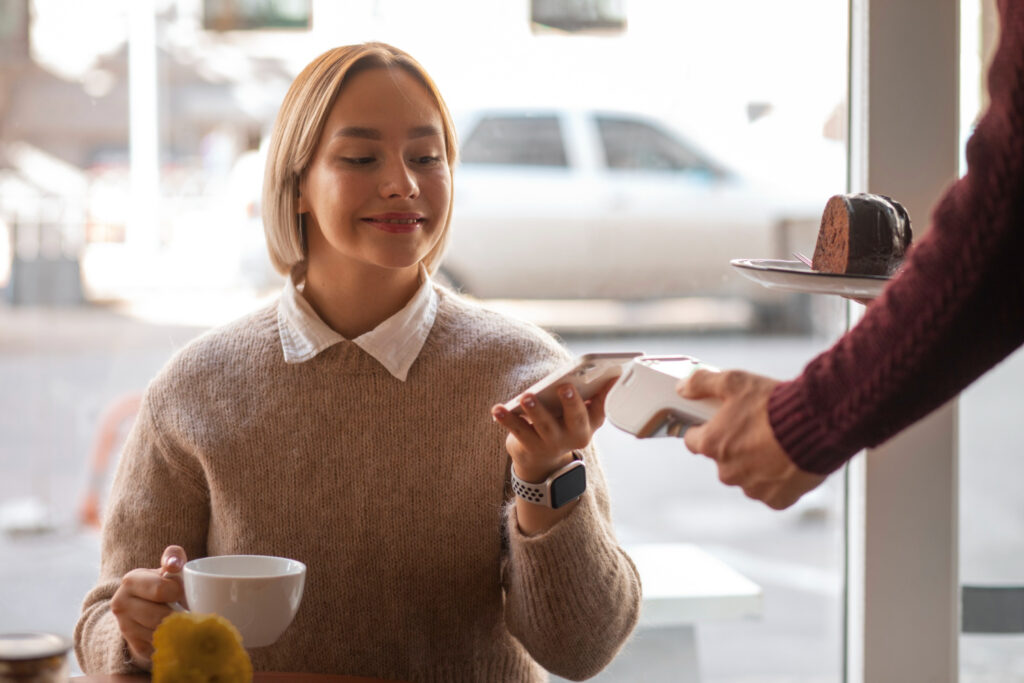 photo-of-woman-paying-for-coffee-and-cake-in-cafe-with-barista-holding-payment-machine