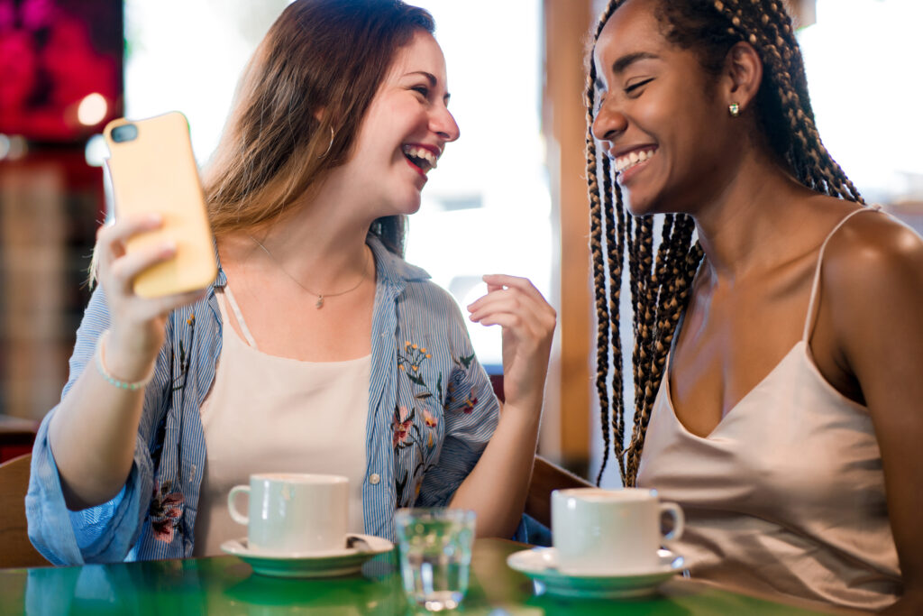 Two-female-friends-laughing-at-a-cafe-in-the-Netherlands-together-being-direct-with-each-other-using-a-mobile-phone