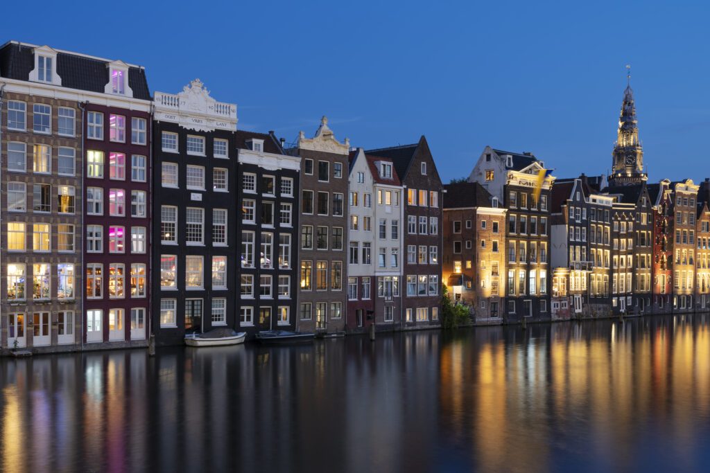 lit-up-amsterdam-houses-next-to-canal-against-night-sky-with-buildings-reflections-in-the-water