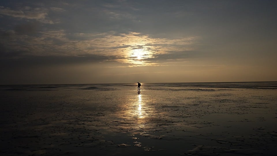 man-walking-on-mudflat-while-sun-is-setting-in-the-wadden-islands