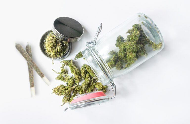 photo-of-amsterdam-weed-buds-spilling-out-of-jar-with-grinder-and-joints-nearby