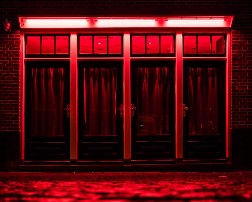 Red Light District in Amsterdam. Red boxes with curtains and wet rainy Cobbles on the street. Place of pleasures.
