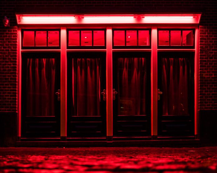 Red Light District in Amsterdam. Red boxes with curtains and wet rainy Cobbles on the street. Place of pleasures.