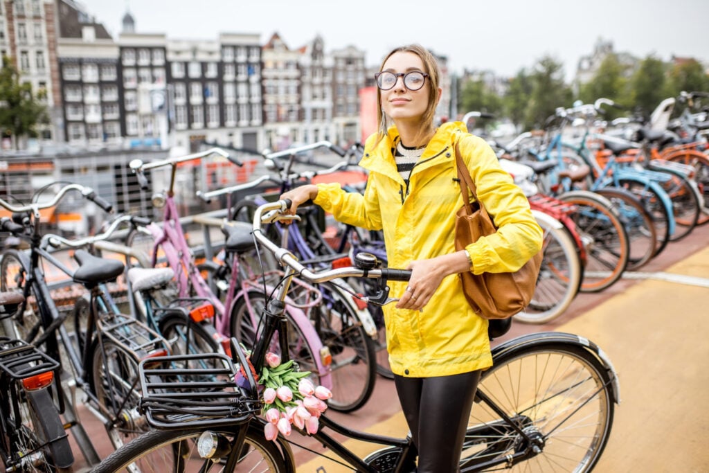 photo-of-woman-in-yellow-raincoat-choosing-bike-in-netherlands-from-many-with-typical-dutch-house-background