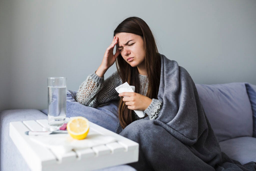 Woman-sick-lying-on-couch-with-blanket-over-her-with-medication-by-her-side