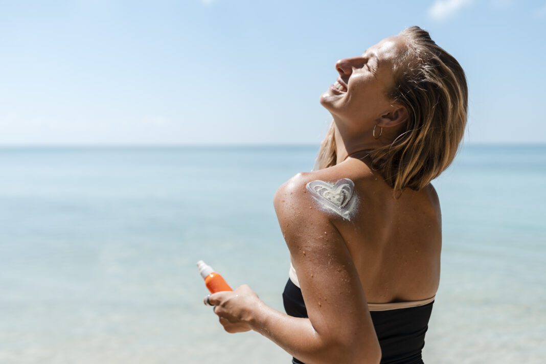 woman-standing-at-the-beach-on-sunny-day-turned-away-from-camera-laughing-with-sunscreen-shaped-like-a-heart-on-her-shoulder