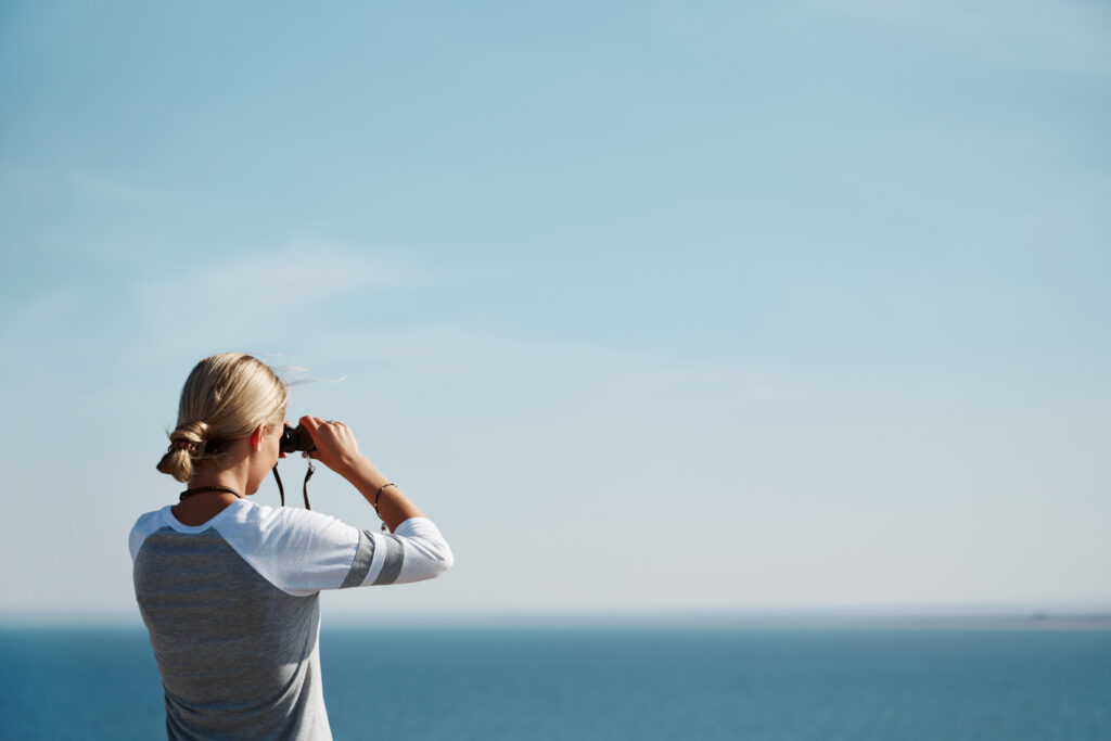 photo of a woman looking through her binoculars at the beach