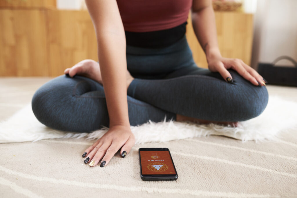 woman-looks-at-a-yoga-app-on-her-phone-whilst-using-a-sim-only-subscription-and-sitting-on-a-mat