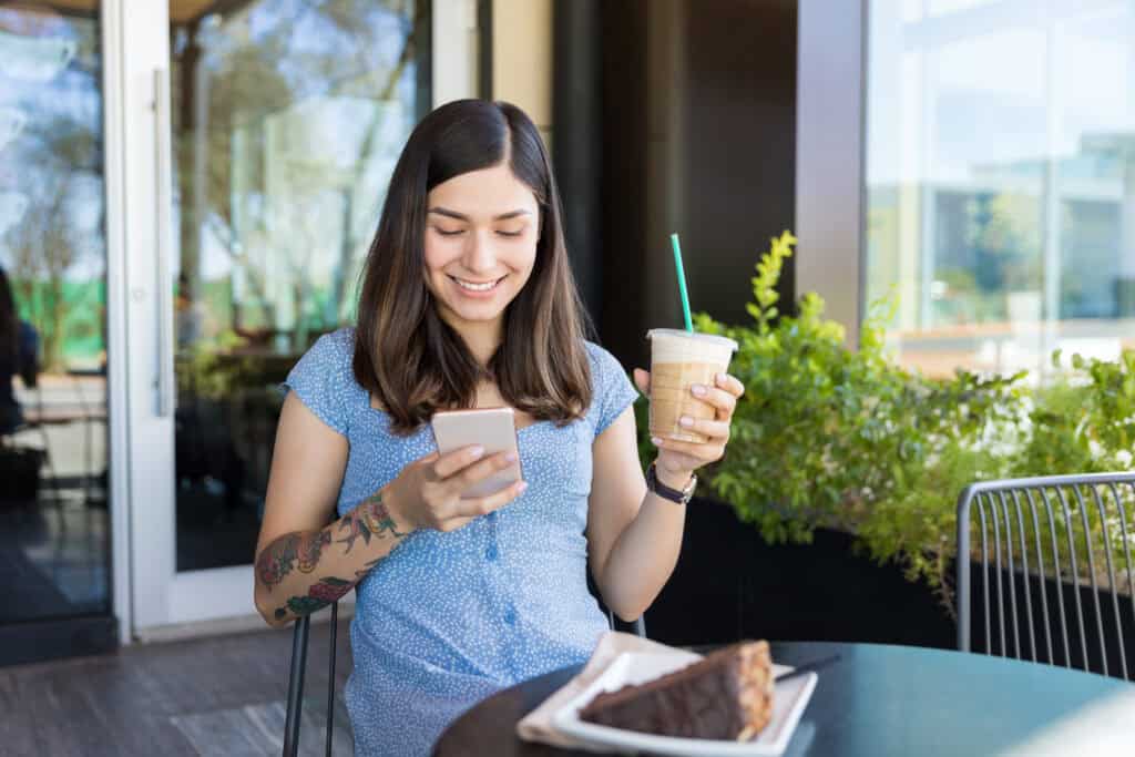 mulher salva ações parciais em seu portfólio de investimentos em um aplicativo móvel enquanto bebe café gelado e come bolo de chocolate