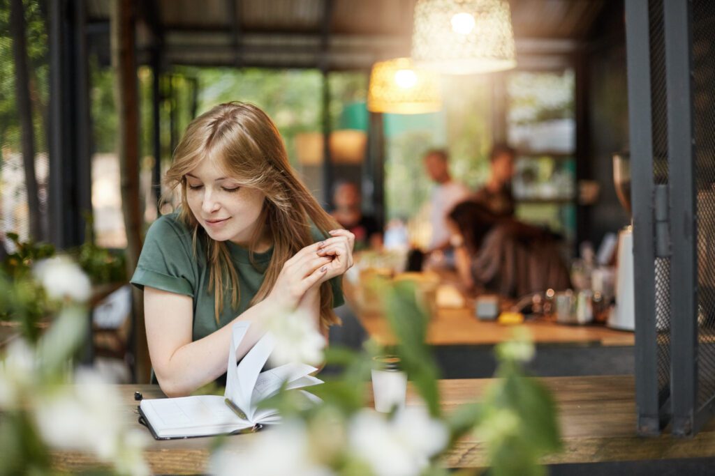 photo-of-a-woman-drinking-coffee-and-looking-at-her-notes-surrounded-by-plants-at-a-cafe