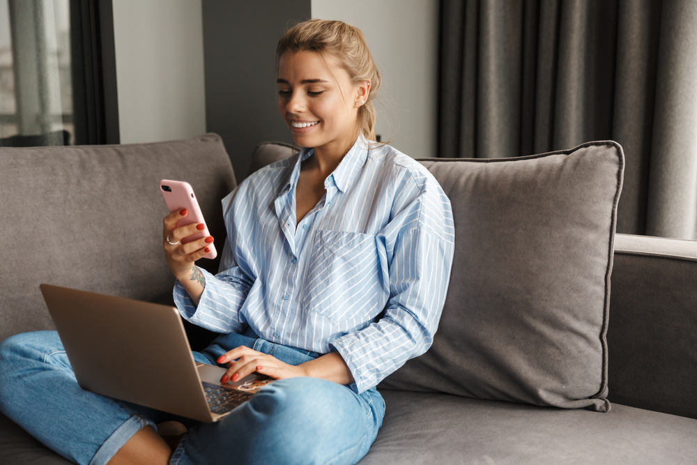 photo-young-woman-sitting-on-couch-using-phone-and-laptop