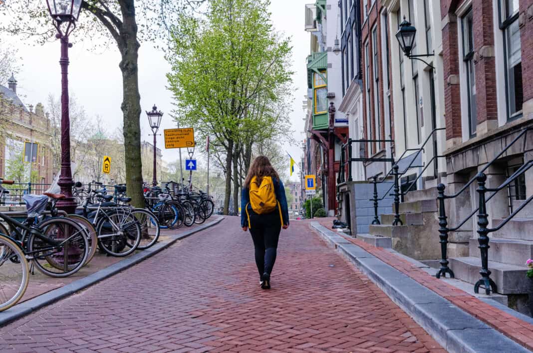 photo-of-woman-walking-alone-on-dutch-amsterdam-streets-wearing-yellow-backpack-walking-away-bad-weather