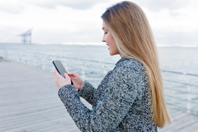 woman-walking-along-dutch-pier-using-esim-on-her-mobile-phone