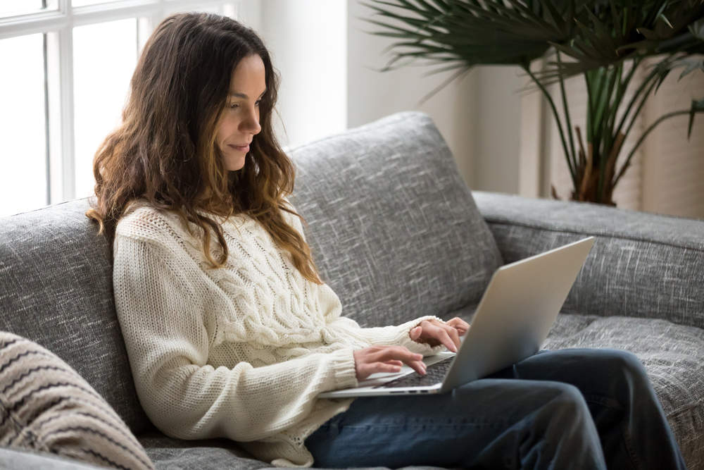 Woman-working-on-her-laptop-while-sitting-on-the-couch-looking-for-nursing-job-in-the-netherlands