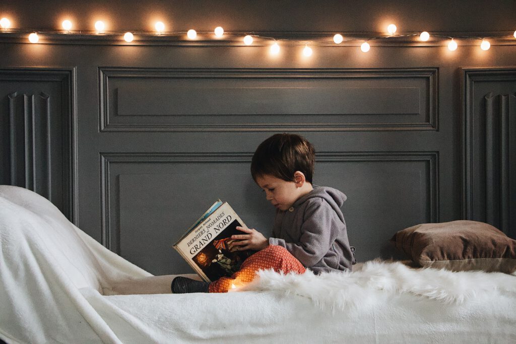 Young-boy-reading-a-French-book-in-his-bed-with-fairylights