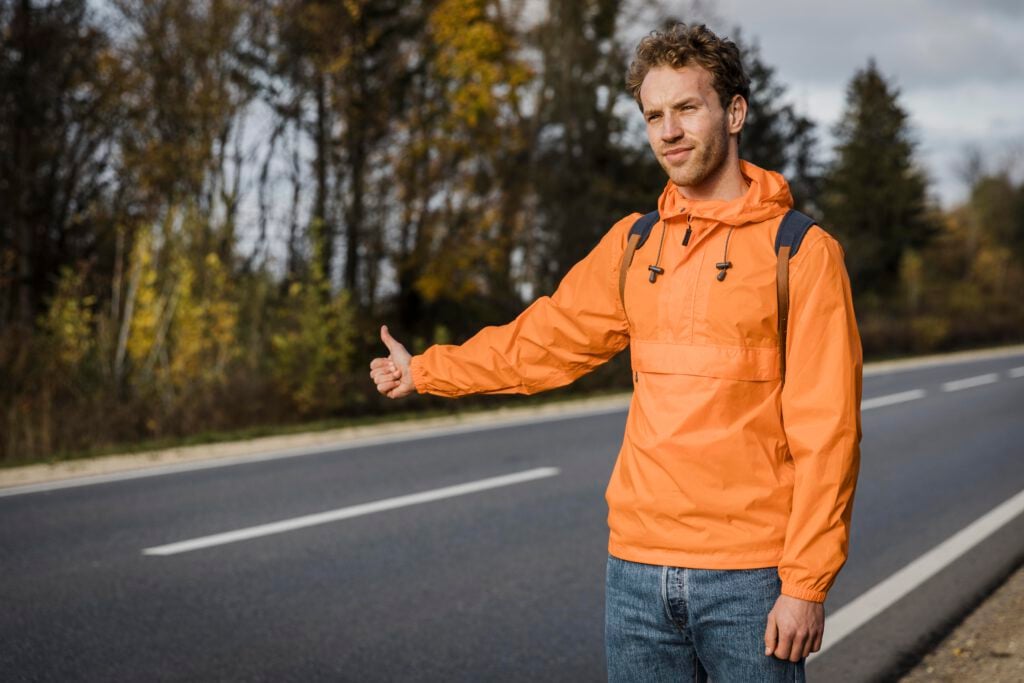 young-man-in-orange-jacket-hitchhiking-near-a-forest-netherlands