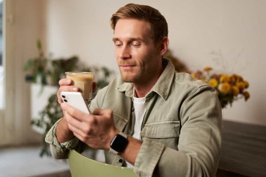 imagem-de-um-homem-jovem-bebendo-café-enquanto-verifica-seus-investimentos-no-telefone