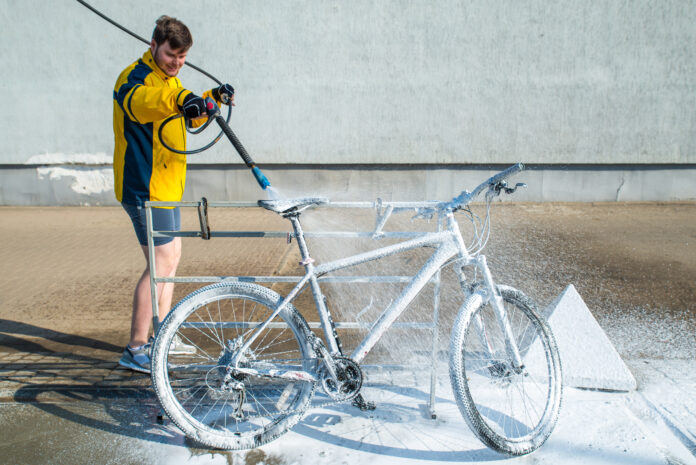young-man-washing-bicycle-with-hose-and-soap