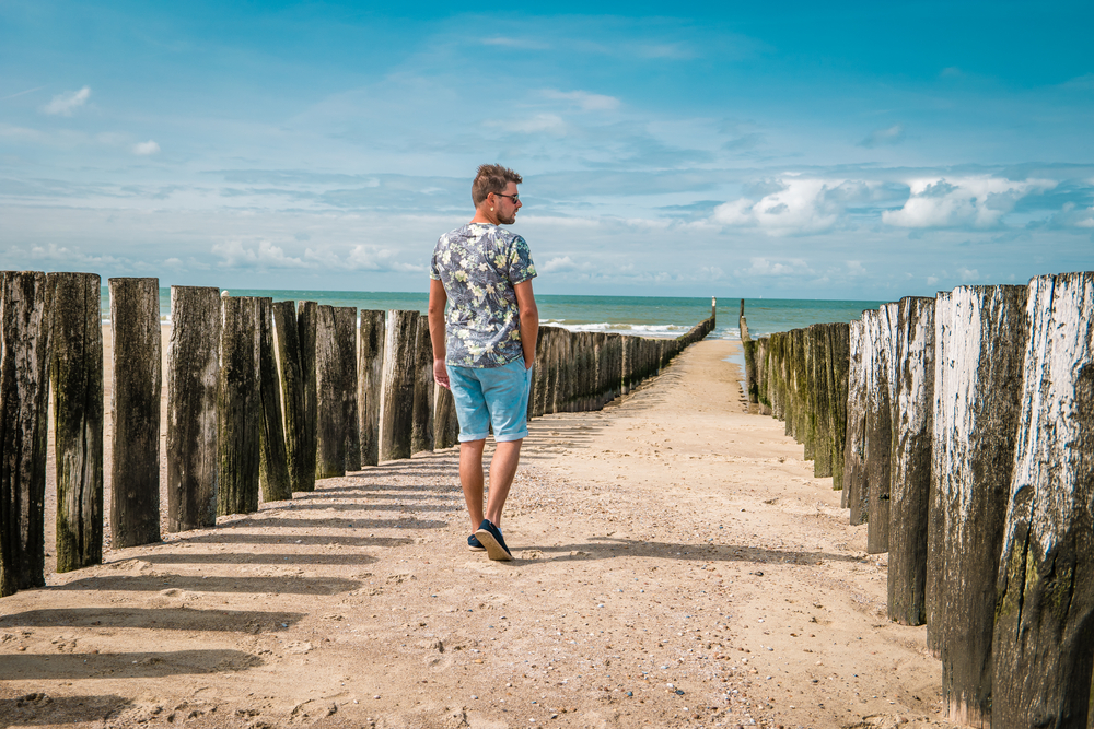 photo-of-man-walking-between-wavebreakers-on-beach-of-domburg-zeeland-with-clouds-in-sky-netherlands