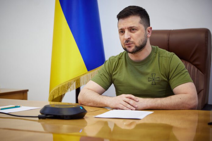 zelensky-in-shirt-sitting-at-desk-ukrainian-flag