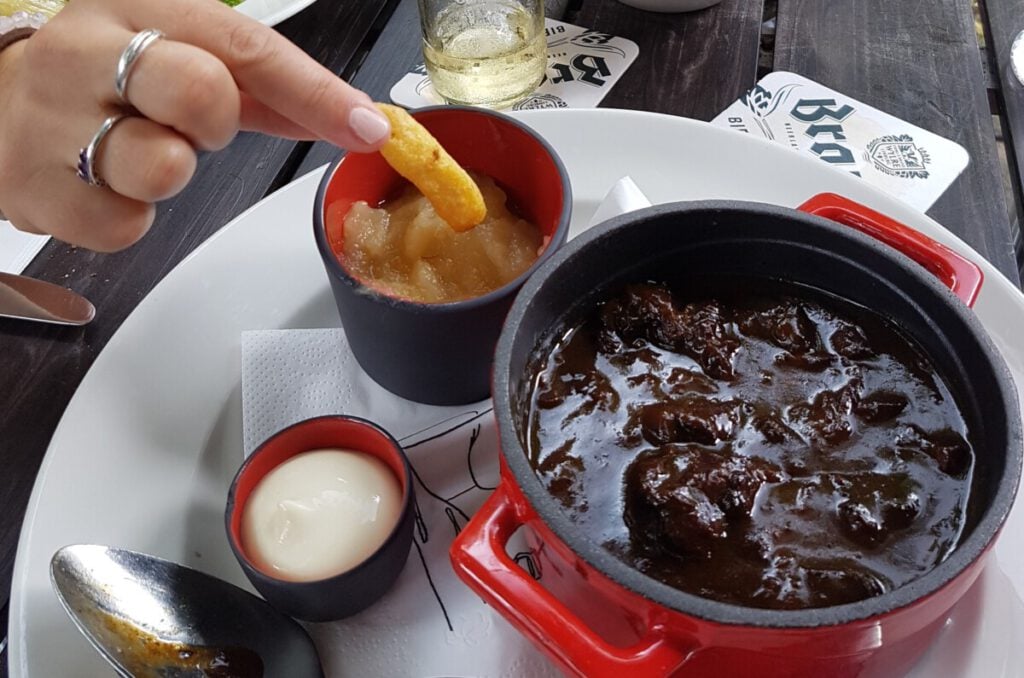 what-to-eat-in-maastricht-beef-stew-with-hand-dipping-a-chip-into-the-stew-and-apple-sauce